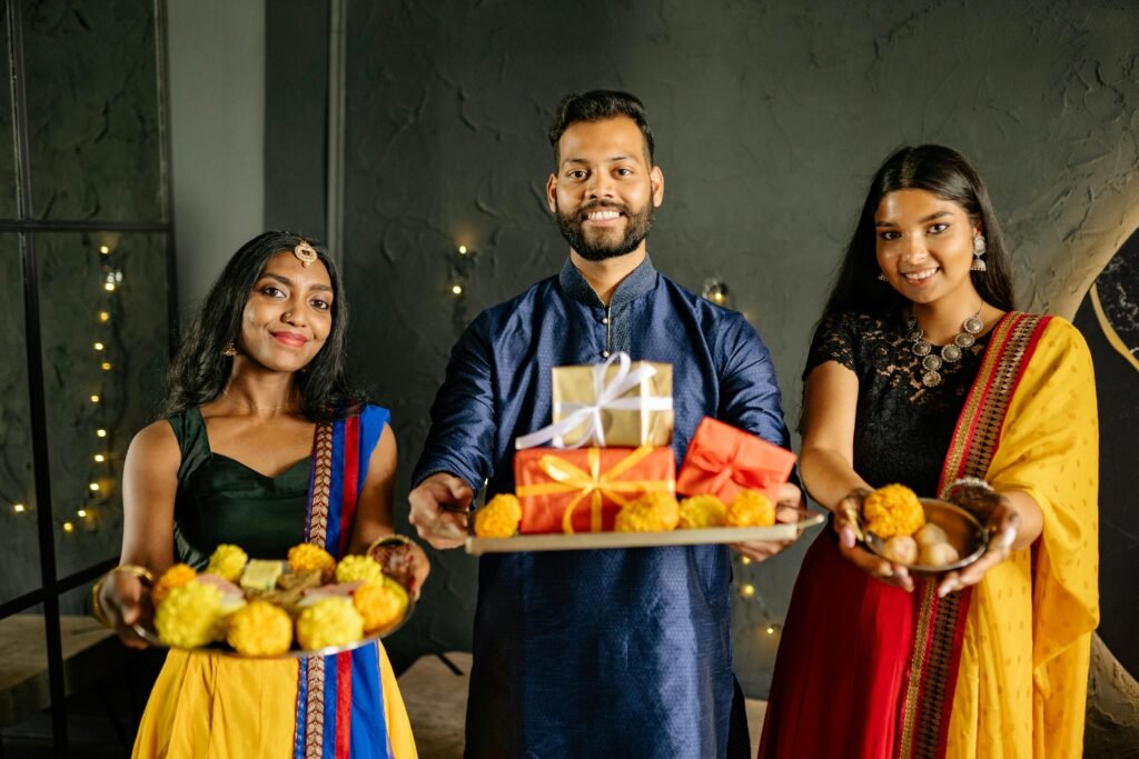 Smiling people in traditional Indian attire holding gifts and marigold flowers for a festive celebration.